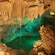 An underground cave with stalactites hanging from the ceiling and a pool surrounded by rock formations